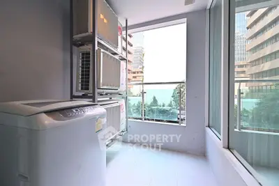 Spacious laundry area with modern washing machine and large windows in urban apartment.