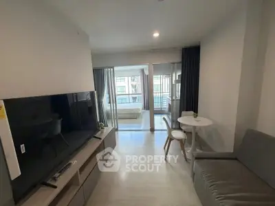 Modern apartment living room with TV, sofa, and dining area leading to a bedroom with balcony view.