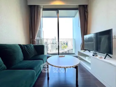 Modern living room with large window and balcony view, featuring a green sofa and flat-screen TV.