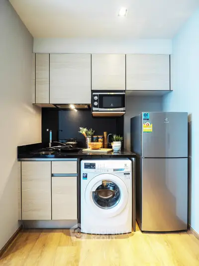 Modern compact kitchen with washing machine, microwave, and fridge in sleek design.