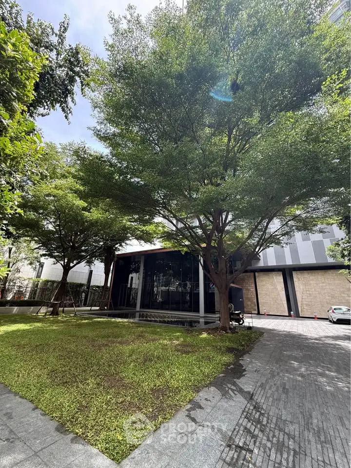 Modern building exterior with lush green garden and paved walkway, perfect for urban living.