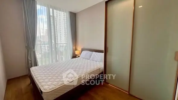 Modern bedroom with large window and wooden flooring in urban apartment.