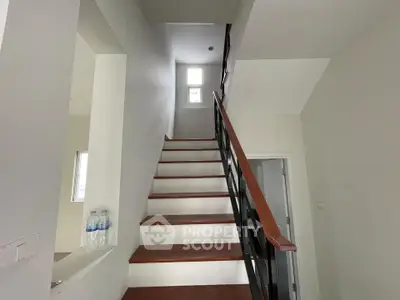 Modern staircase with wooden steps and sleek railing in a bright, minimalist home interior.
