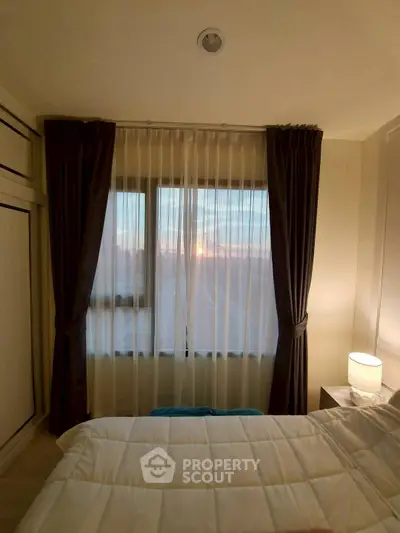 Cozy bedroom with sunset view through elegant curtains, featuring a comfortable bed and soft lighting.