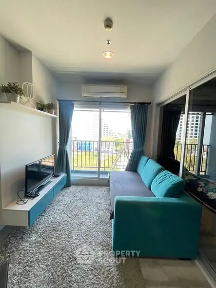 Modern living room with teal sofa and balcony view in urban apartment.