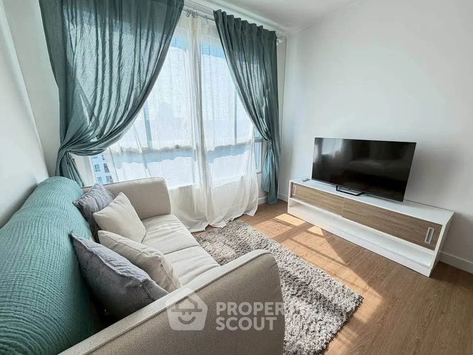 Bright and cozy living room with modern sofa and TV, featuring large windows and elegant curtains.