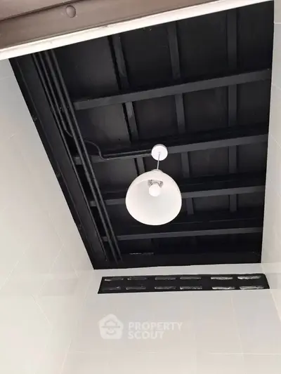 Modern ceiling design with exposed black beams and white pendant light in a stylish interior space.