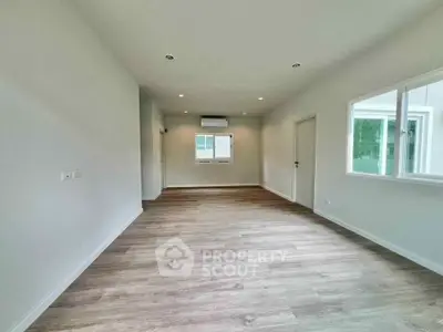 Spacious empty room with wooden flooring and large windows in modern apartment.