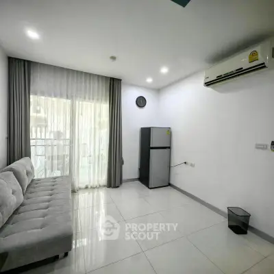 Modern living room with sleek sofa, fridge, and air conditioning in a bright apartment.