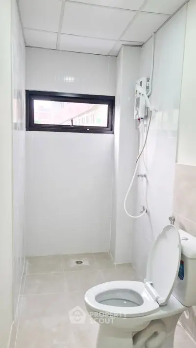 Modern bathroom with white tiles and compact shower area, featuring a sleek toilet and window for natural light.