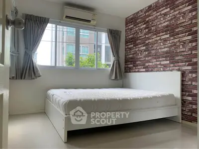 Modern bedroom with brick accent wall and large window in urban apartment.