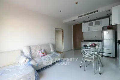 Modern open-layout living room with kitchen, featuring sleek furniture and bright natural lighting.