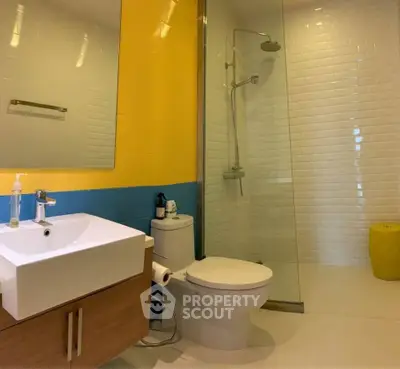Modern bathroom with glass shower, vibrant yellow and blue tiles, and sleek fixtures.