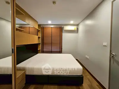 Modern bedroom with wooden flooring and built-in shelves, featuring a comfortable bed and air conditioning.
