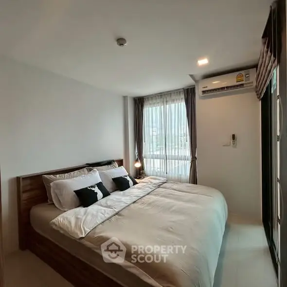 Modern bedroom with large window and stylish decor in urban apartment.