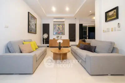Spacious and modern living room with sleek grey sofas, vibrant throw pillows, and a stylish wooden coffee table, complemented by elegant wall art and pristine white flooring.