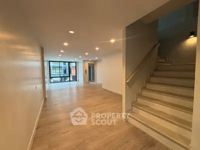 Spacious modern living room with wooden flooring and staircase, featuring large windows for natural light.