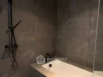 Modern bathroom with sleek dark tiles and a built-in bathtub featuring contemporary fixtures.