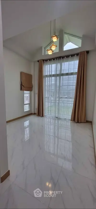 Spacious living room with high ceiling and large windows, featuring elegant lighting and marble flooring.