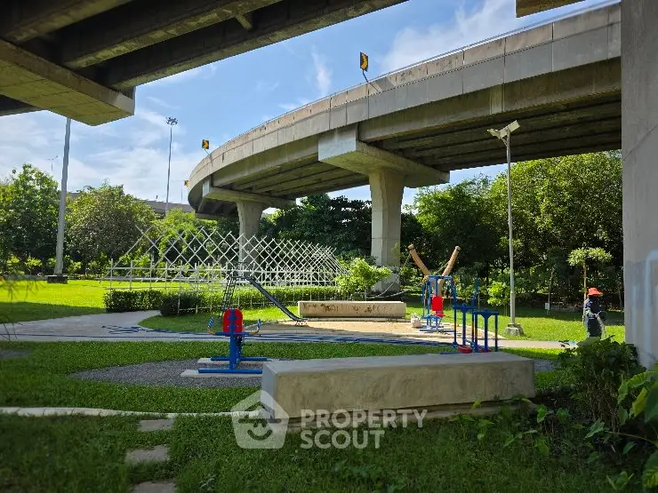 Urban park under highway with playground and greenery, ideal for family recreation and relaxation.