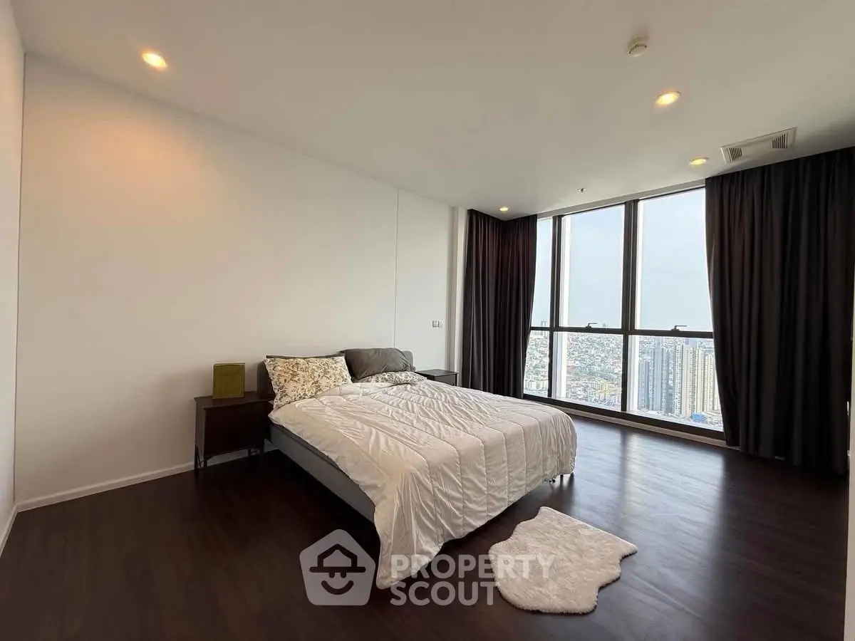 Spacious bedroom with large windows offering stunning city views, featuring elegant hardwood floors and modern decor.