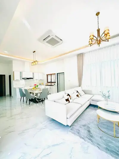 Luxurious open-plan living room with elegant decor and modern kitchen, featuring marble flooring and chic lighting.