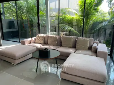 Spacious living room with modern sofa and lush garden view through glass doors.