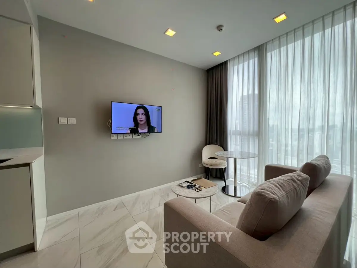Modern living room with TV, cozy sofa, and city view through large windows.