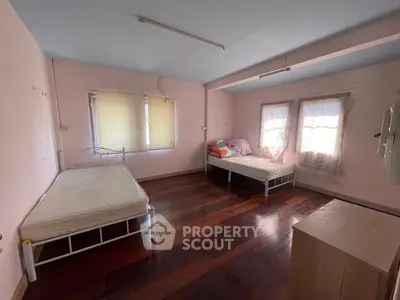 Spacious bedroom with wooden floors and natural light, featuring two single beds and large windows.
