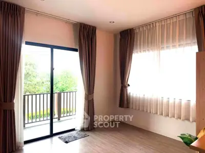 Bright living room with large windows and balcony access, featuring elegant curtains and wooden flooring.