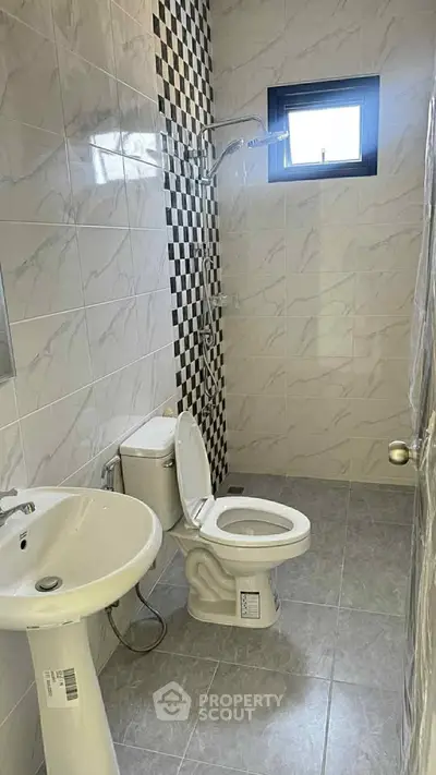 Modern bathroom with sleek tiles and contemporary fixtures, featuring a shower and natural light window.