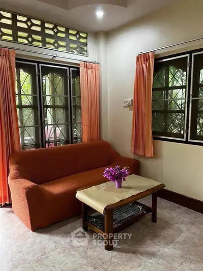 Cozy living room with orange sofa and natural light from large windows.