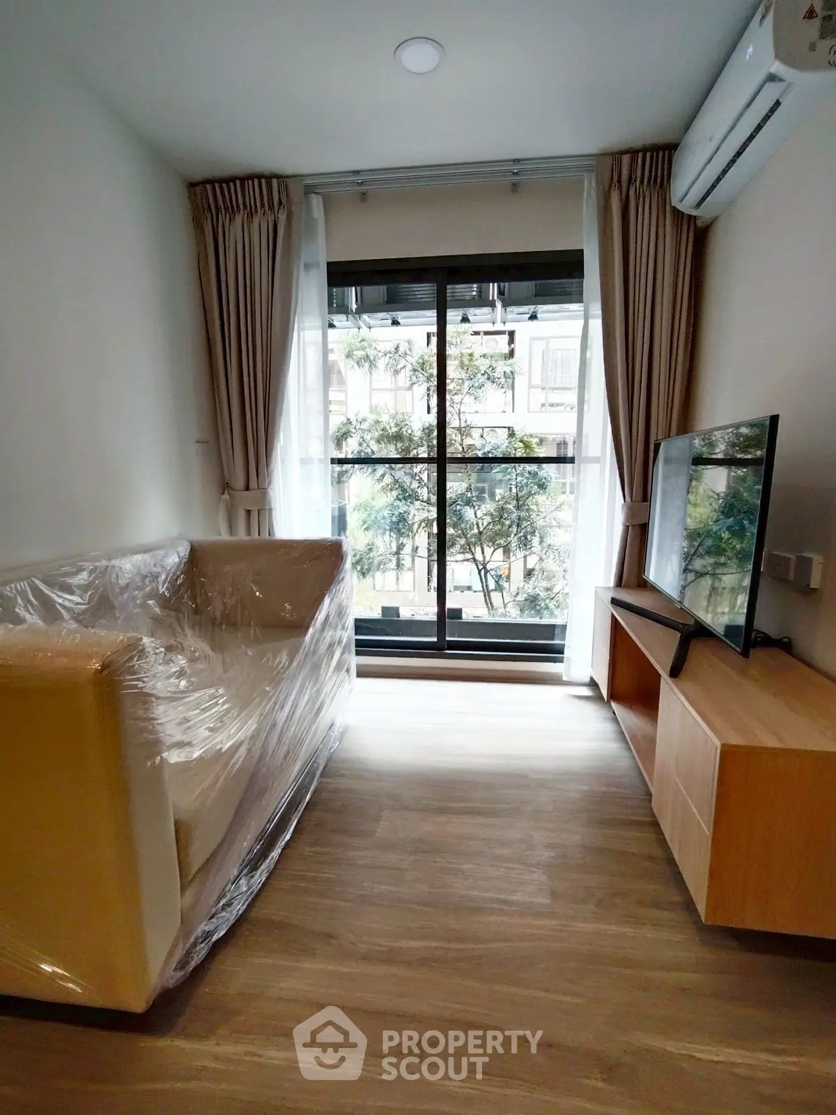 Modern living room with large window and air conditioning, featuring a sofa and TV stand.