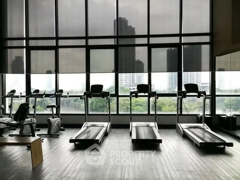 Modern gym with treadmills and city view through large windows.