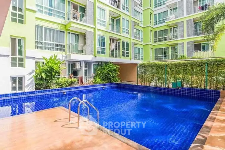 Modern apartment building with a vibrant blue swimming pool and lush greenery.
