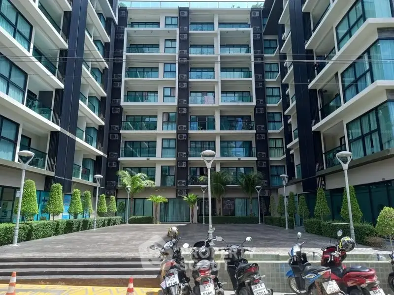 Modern apartment building exterior with lush landscaping and parked scooters in front.