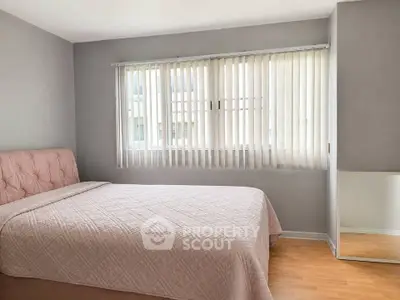 Cozy bedroom with soft pink bedding and large window with vertical blinds, perfect for relaxation.