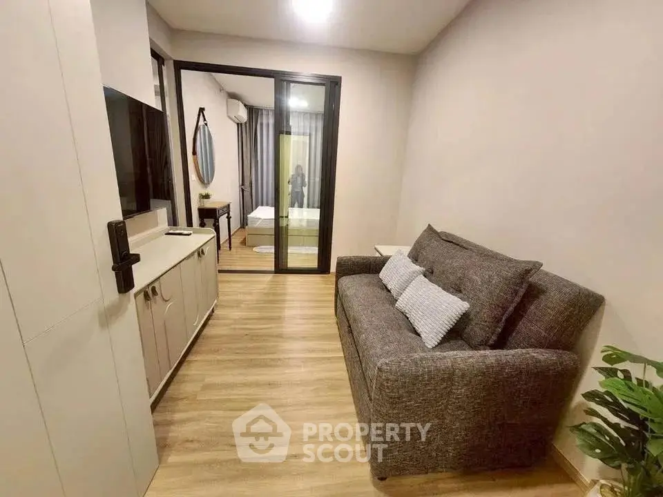 Modern compact living room with sofa and view into bedroom, featuring sleek wooden flooring and contemporary decor.