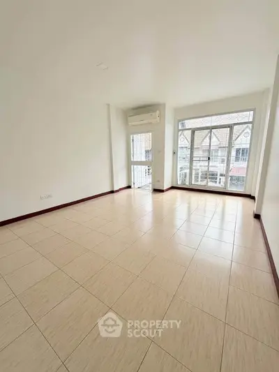 Spacious empty living room with large windows and tiled flooring in modern apartment.