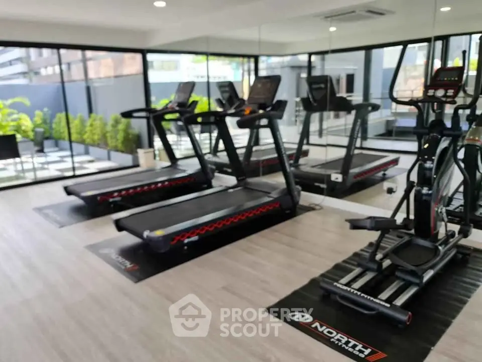 Modern gym with treadmills and exercise equipment in a bright, spacious room with large windows.