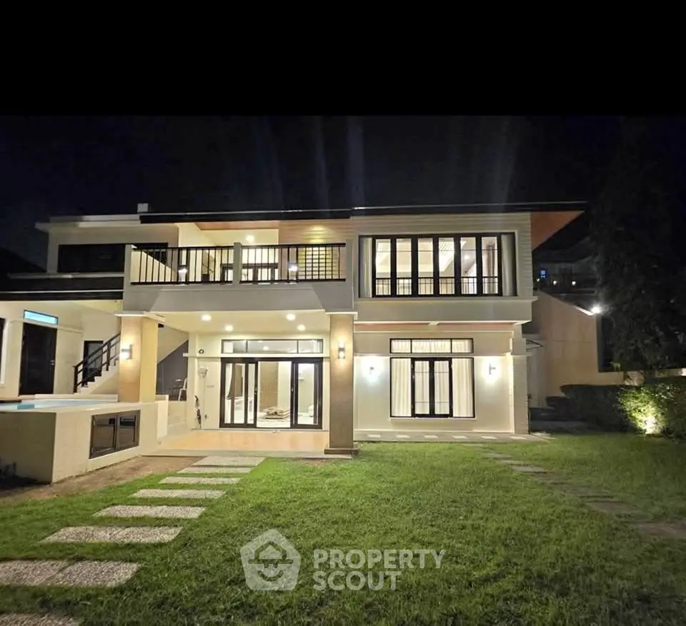 Luxurious modern two-story house with elegant lighting and spacious lawn at night.