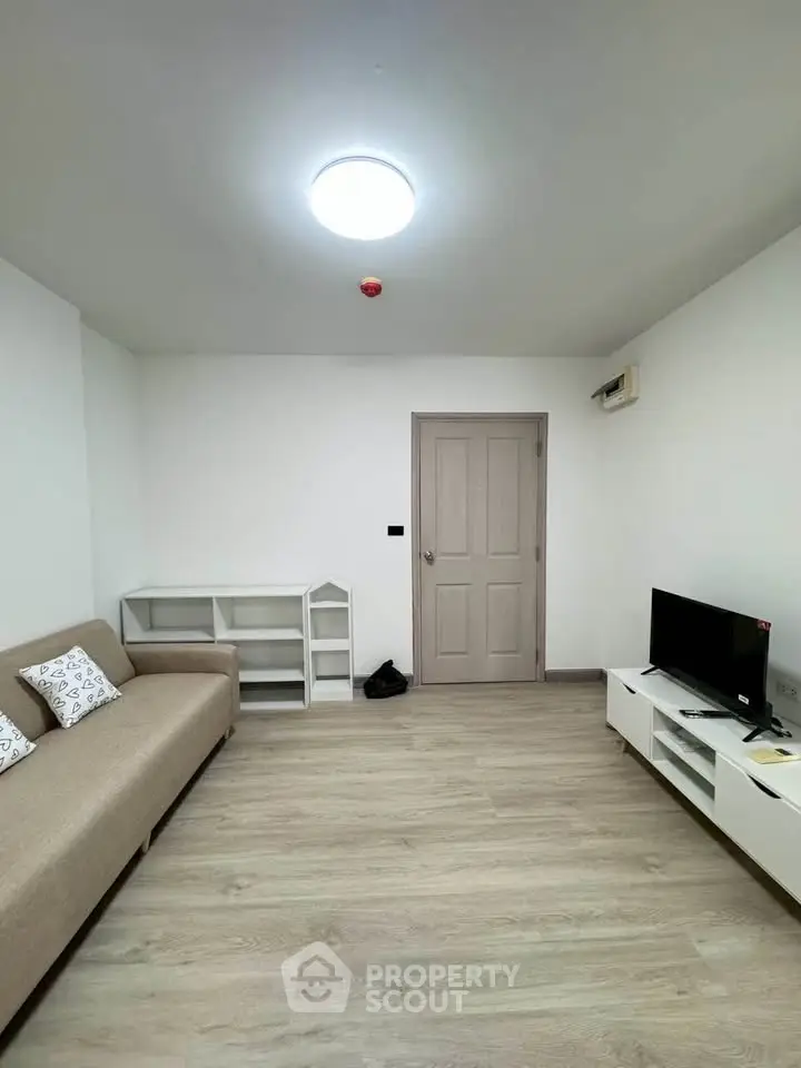 Modern living room with minimalist decor, featuring a beige sofa, TV unit, and sleek wooden flooring.