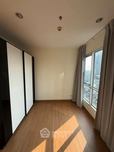Bright bedroom with large windows and city view, featuring modern wardrobe and wooden flooring.