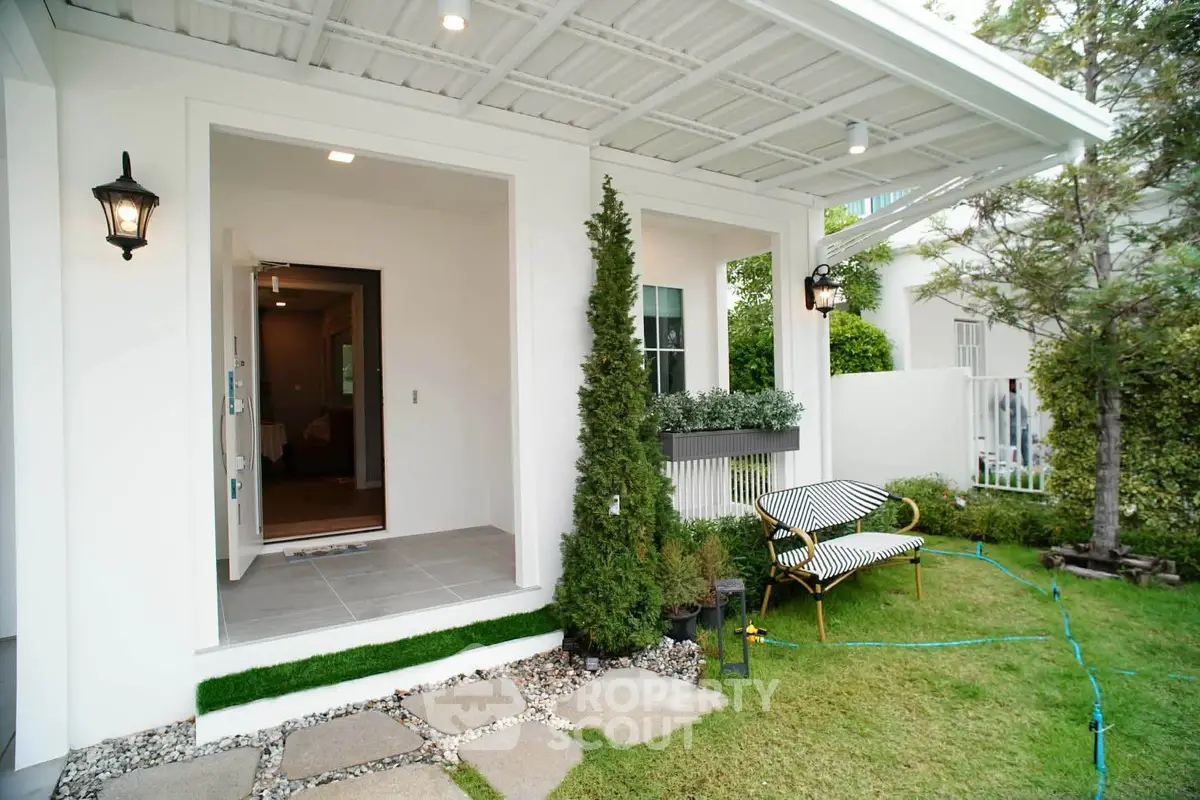 Charming modern home entrance with lush garden and cozy outdoor seating area.