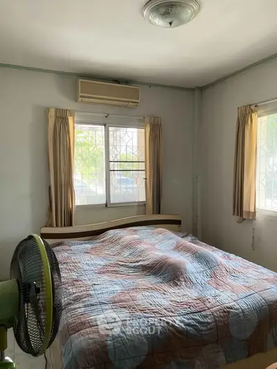 Cozy bedroom with air conditioning and natural light, featuring a comfortable bed and fan.