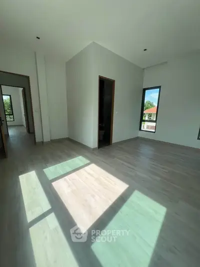 Spacious sunlit room with modern flooring and large windows offering scenic views.