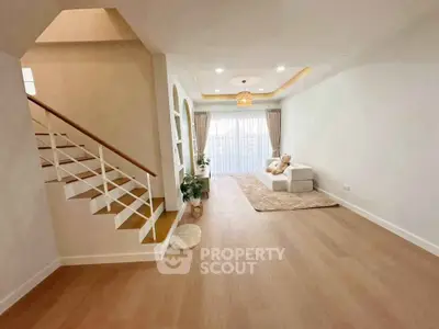 Spacious living room with modern decor and natural light, featuring a cozy seating area and elegant staircase.