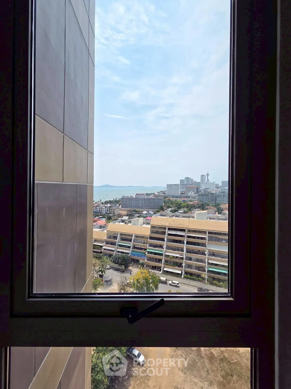 Stunning cityscape view from a high-rise window overlooking urban skyline and distant sea.