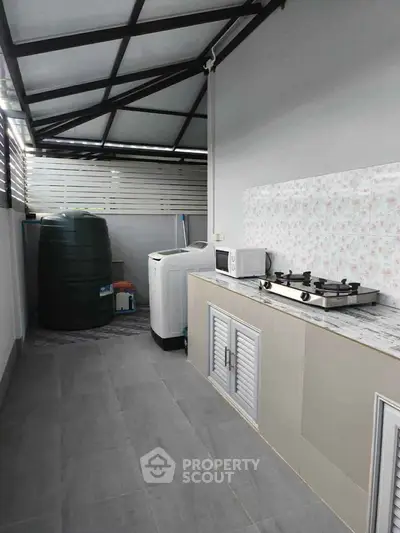 Modern outdoor kitchen with gas stove and washing machine in covered area.