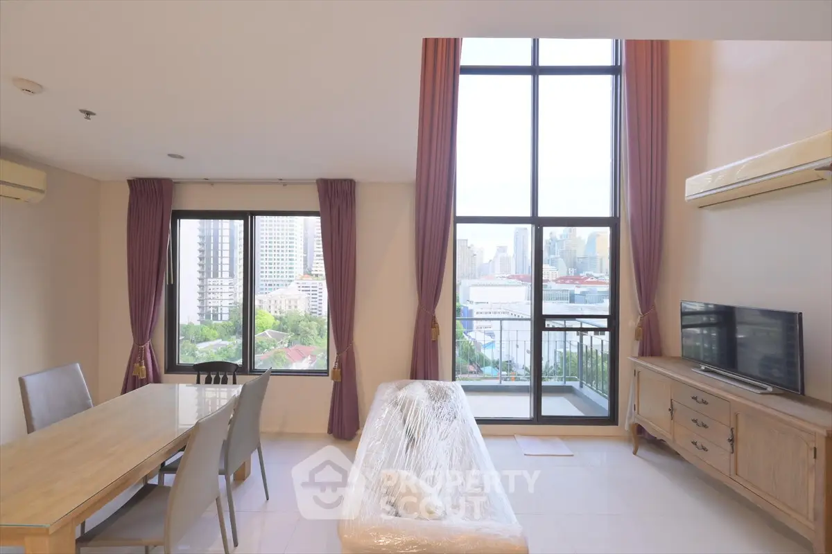 Spacious living room with high ceilings and city view, featuring modern furniture and large windows.